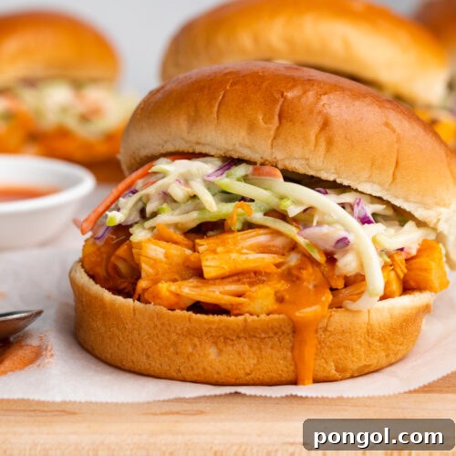 Close-up of a single Buffalo Jackfruit Sandwich, showing the shredded jackfruit and creamy coleslaw filling, nestled in a toasted bun.