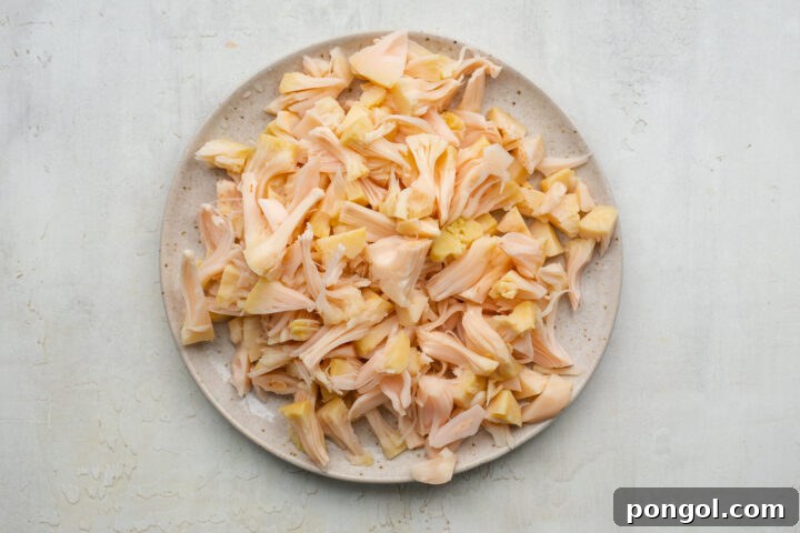 Hand-pulled shredded jackfruit on a white plate, ready for cooking.