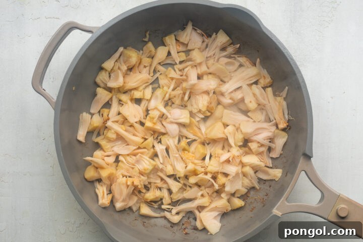 Shredded jackfruit browning in a large skillet with neutral oil.