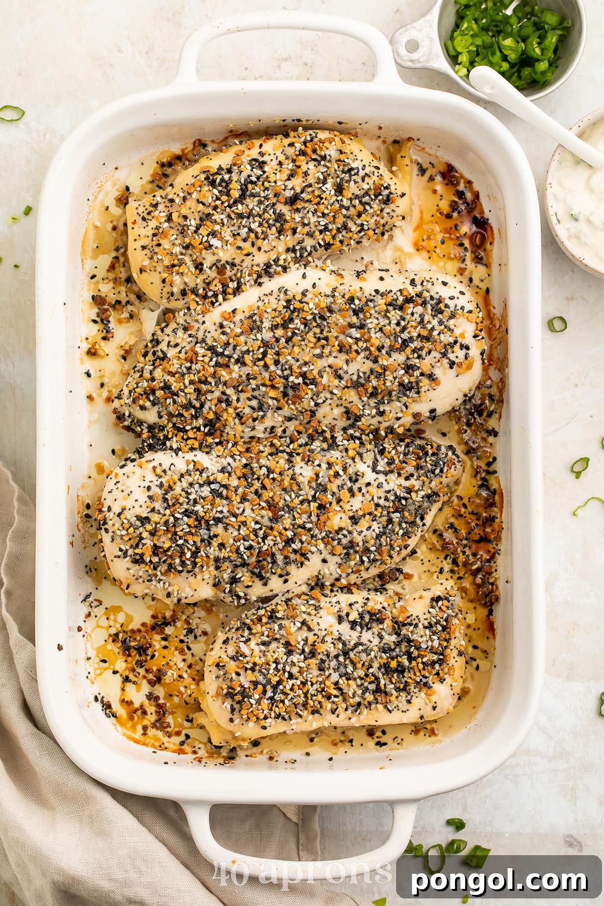 Four perfectly cooked Whole30 Everything Bagel chicken breasts resting in a white rectangular casserole dish on a rustic wooden table.