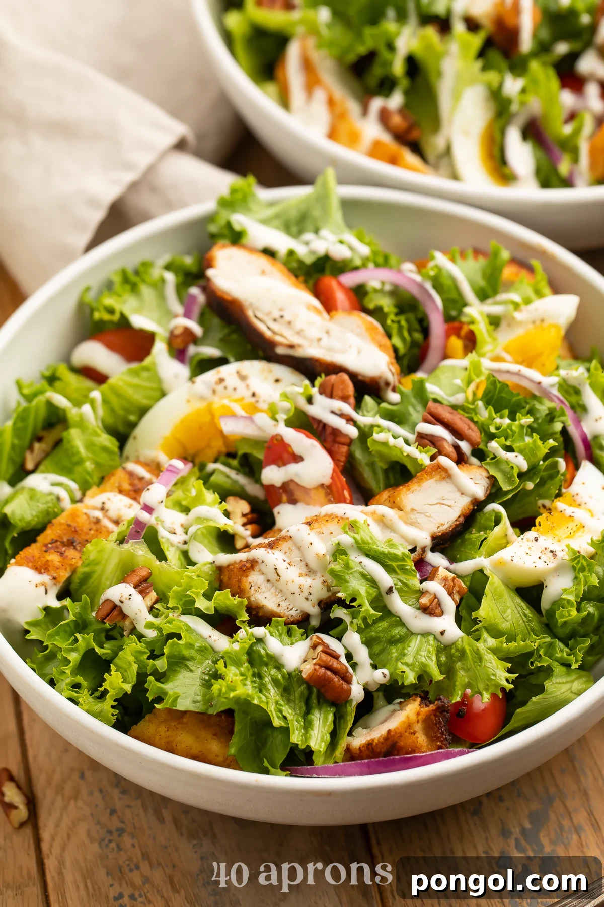 Fresh green salad topped with red onion, strips of fried chicken, tomatoes, pecans, and eggs.