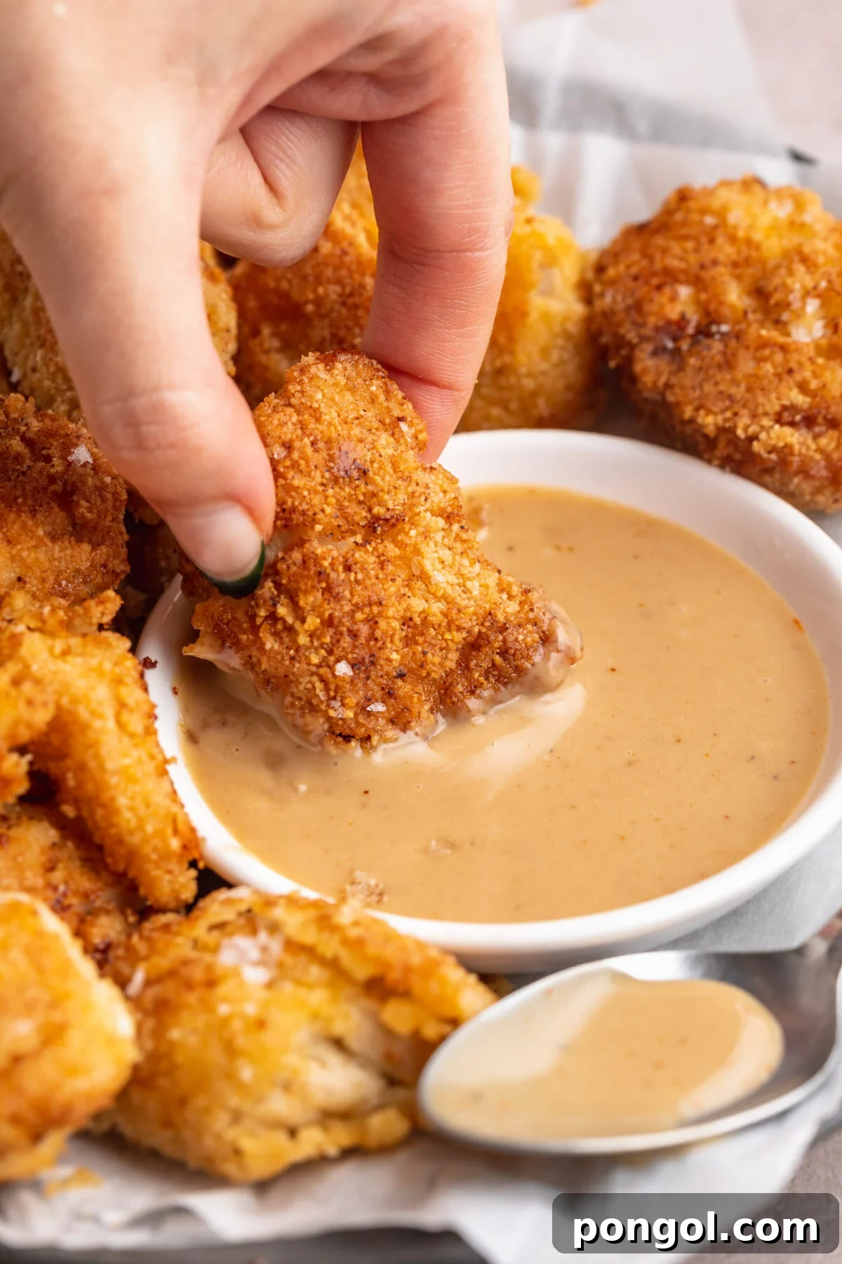 A hand dipping a keto chicken nugget into a small ramekin of keto honey mustard sauce.