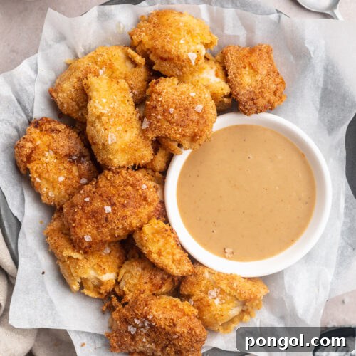Overhead view of a plate, lined with parchment paper, holding keto chicken nuggets and a ramekin of keto honey mustard sauce.
