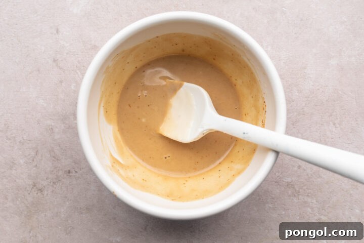 Keto honey mustard sauce in a small white mixing bowl with a white silicone spatula.