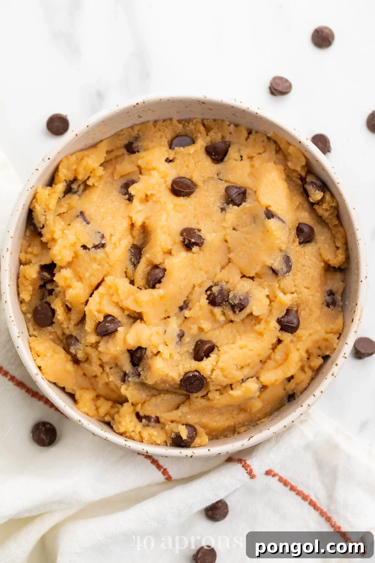 Keto cookie dough in a large bowl with keto chocolate chips sprinkled around the bowl, ready to satisfy any sweet tooth.