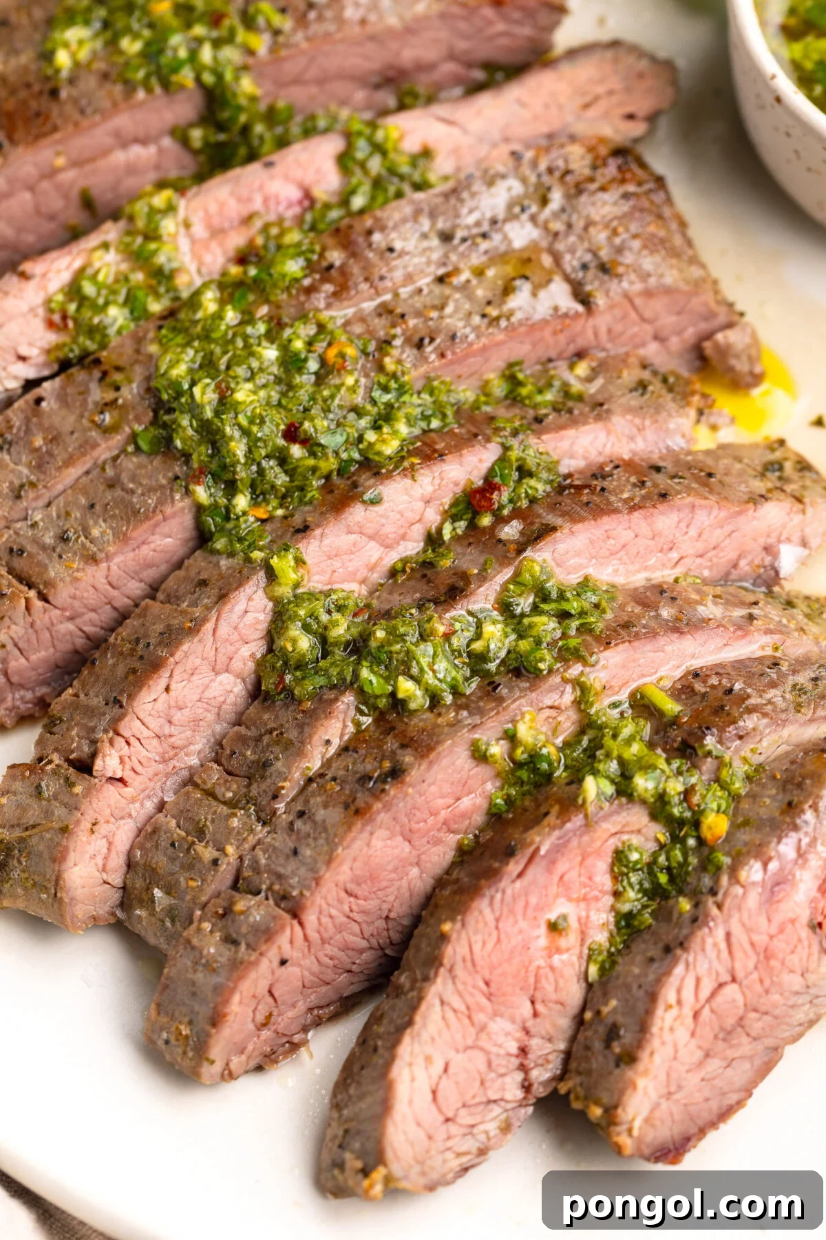 Sous vide flank steak, sliced thin and topped with fresh green chimichurri resting on a platter, ready to be served.