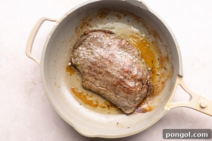 Seared flank steak sizzling in a large skillet with oil.