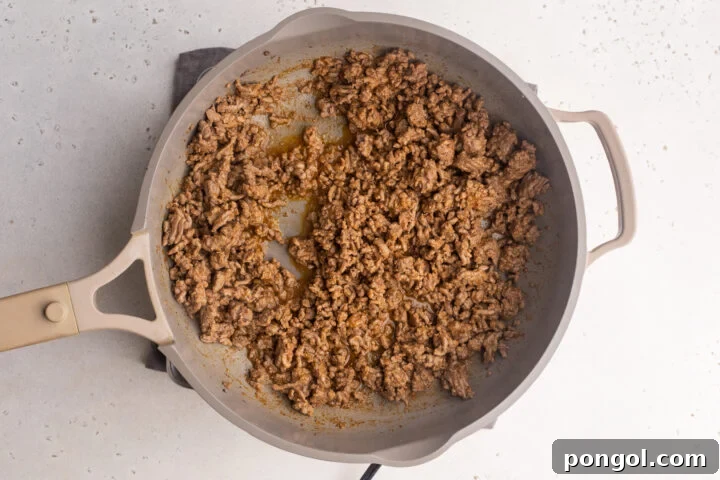 Ground beef with keto taco seasoning and liquid simmering in a large skillet.