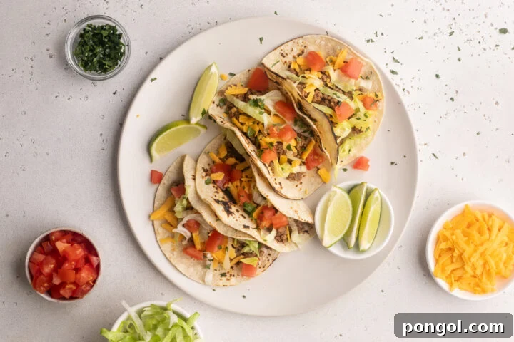 Finished keto tacos on a plate with fresh toppings, lime wedges, and bowls of garnish surrounding.