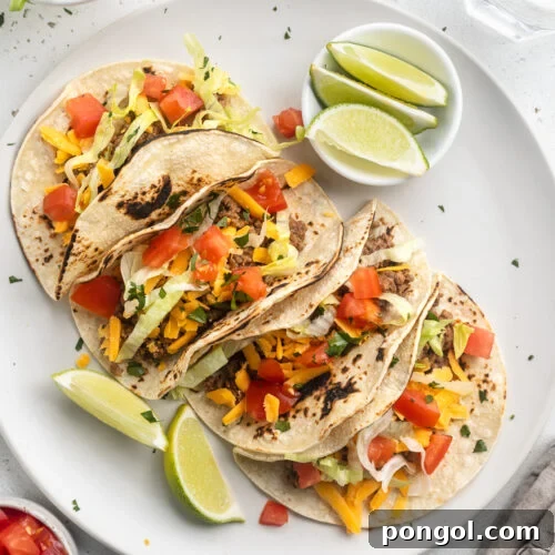 4 keto tacos in homemade keto tortillas lined up on a round white plate with lime wedges and toppings around them.
