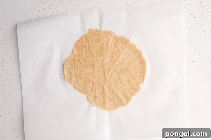 Keto taco tortilla dough expertly rolled into a perfect tortilla shape on a sheet of parchment paper.