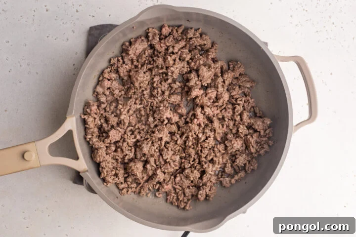 Ground beef browning in a large skillet, ready for seasoning.