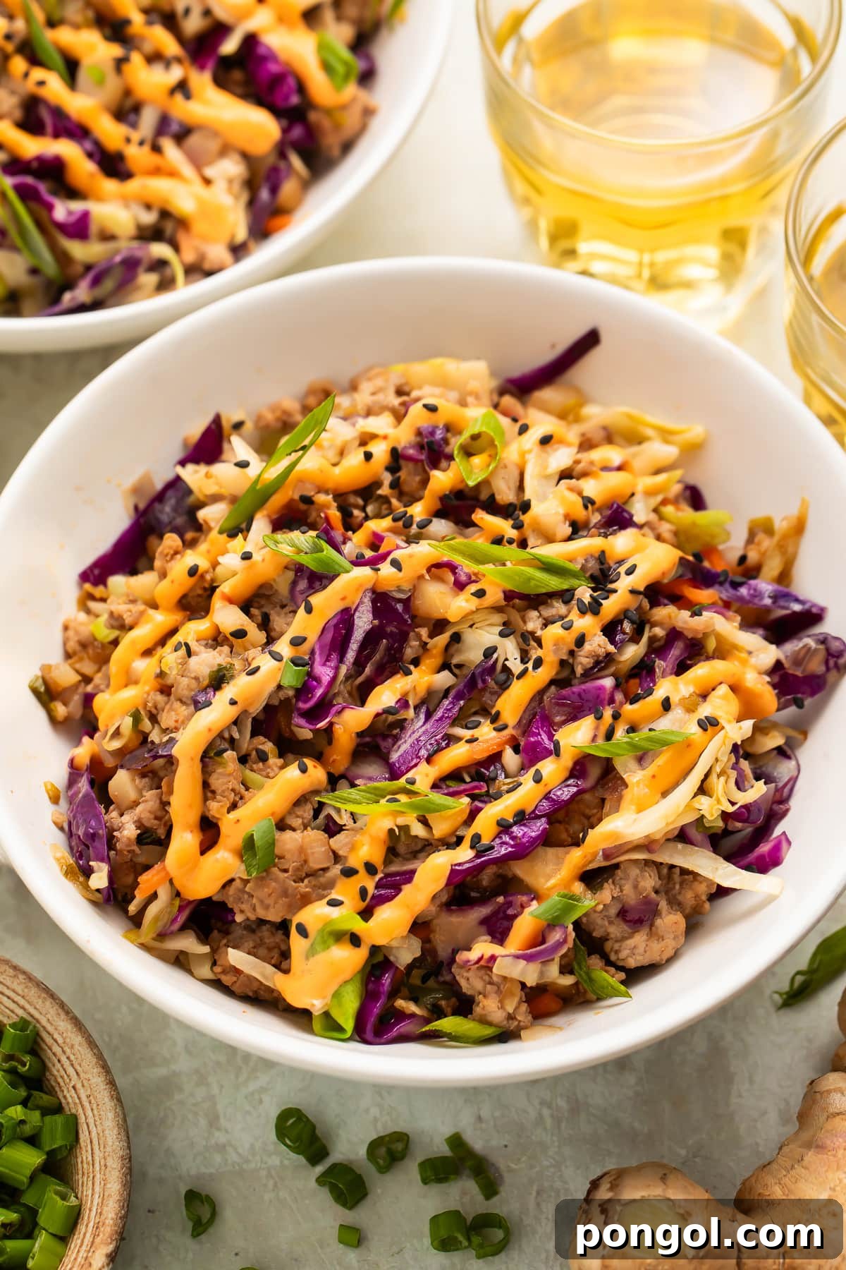 Overhead view of two white bowls filled with Whole30 egg roll mixture topped with orange creamy chili sauce and black sesame seeds.