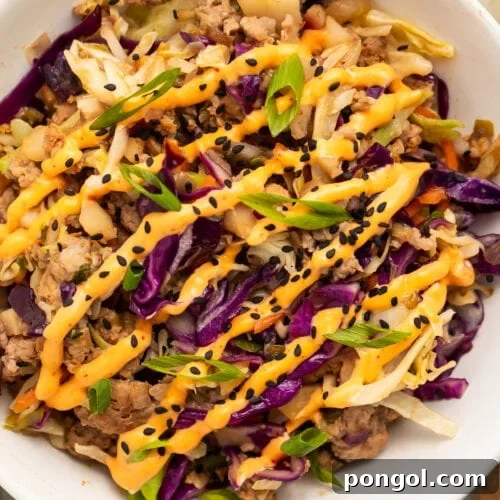 Close-up of egg roll in a bowl with ground pork, purple cabbage, and green onions drizzled with spicy orange sauce and black sesame seeds