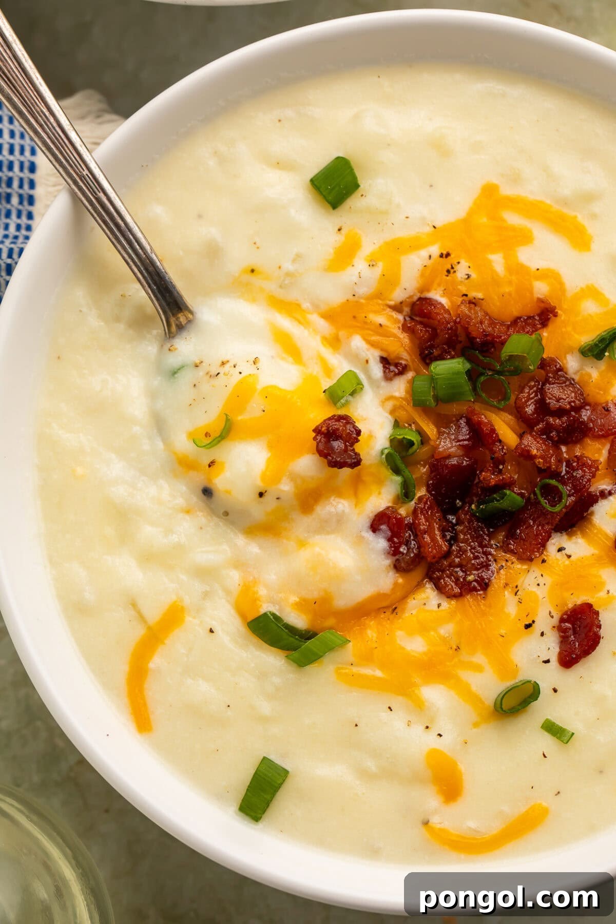 Creamy Country Potato Soup 4 An inviting close-up overhead view of creamy potato soup served in a pristine white bowl, beautifully adorned with melted cheese, crumbled bacon, and vibrant green onions.