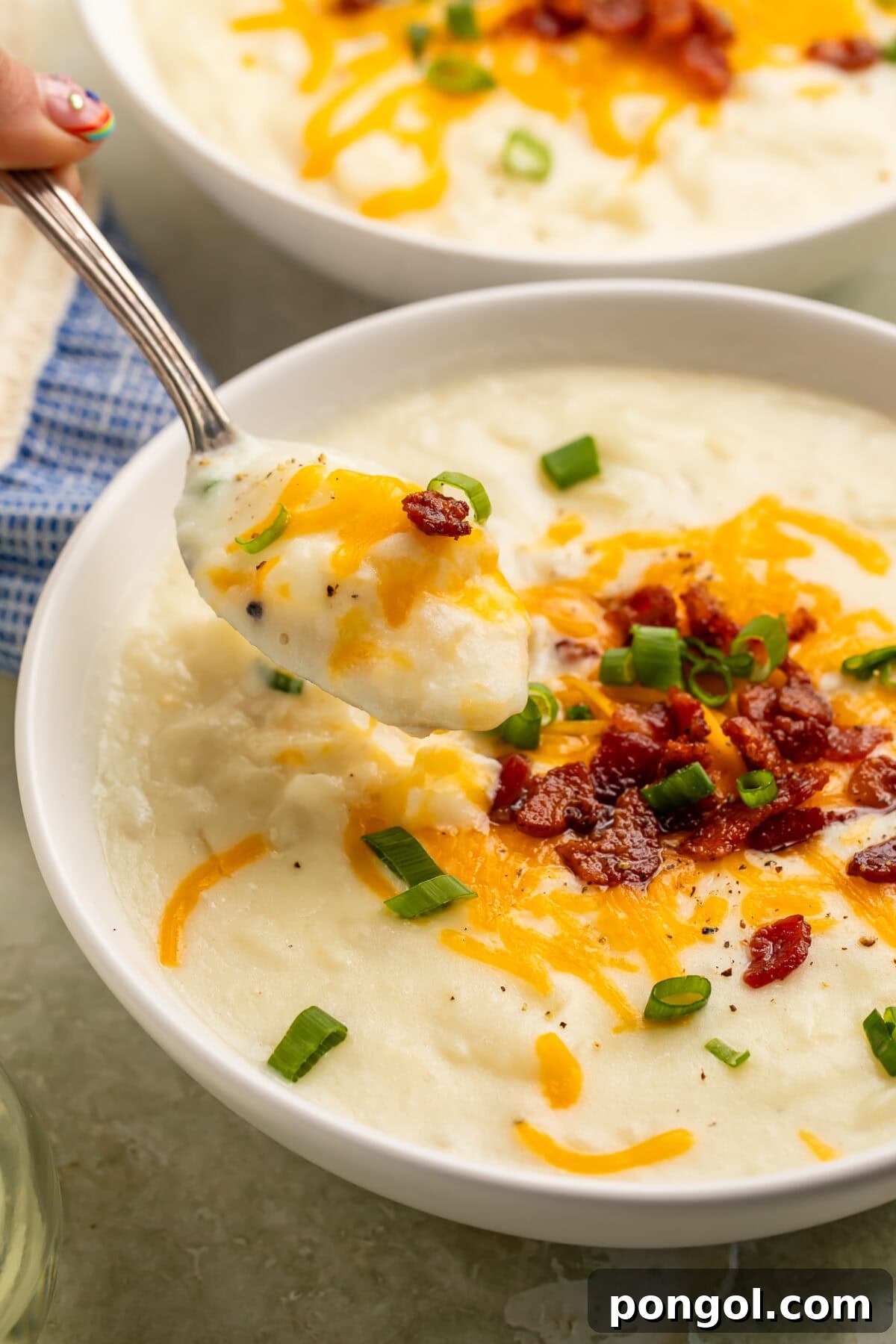 Creamy Country Potato Soup 5 Two pristine white bowls of creamy potato soup, elegantly garnished with cheese and bacon, resting on a rustic wooden table alongside refreshing water glasses, setting a cozy dinner scene.