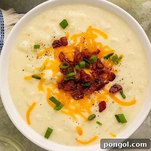 Creamy old-fashioned potato soup in a white bowl topped with shredded cheddar cheese, bacon, and green onions.
