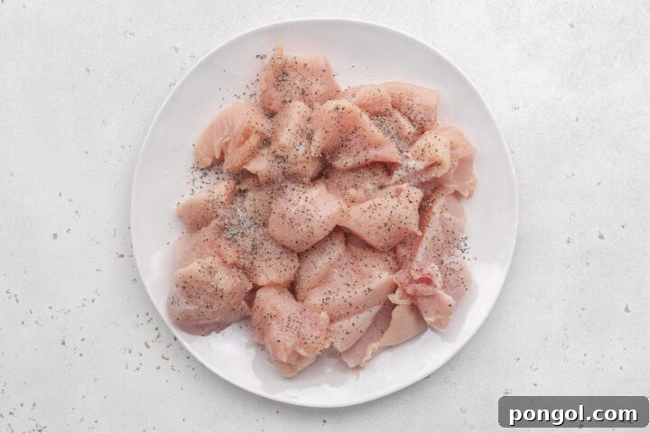 Boneless, skinless chicken breasts cut into 1-inch cubes and piled on a white plate ahead of marinating.