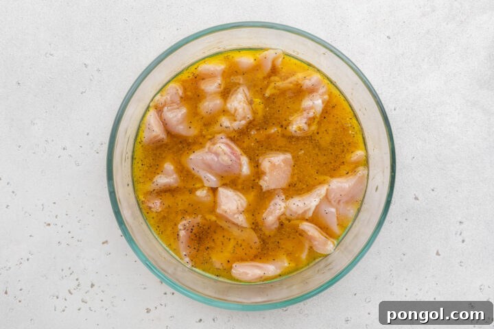 Boneless, skinless chicken breast chunks marinating in a mixture of white wine, olive oil, and lemon juice in a large glass mixing bowl.