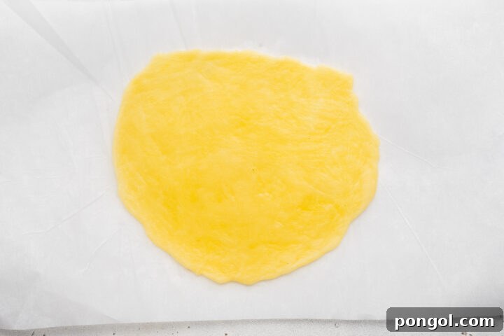 Keto egg noodle rolled flat on a sheet of parchment paper