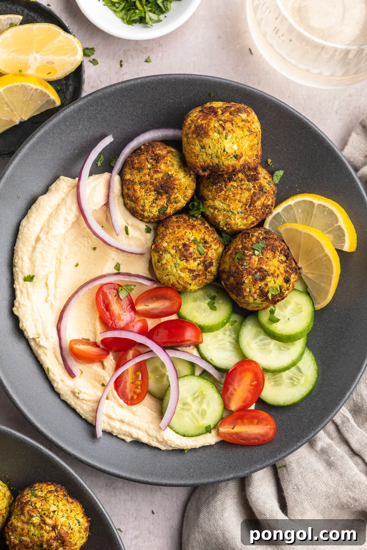 Golden Crispy Air Fryer Falafel 2 Overhead view of a bowl of air fryer falafel with a cucumber and tomato salad on a table with a napkin.