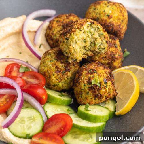Overhead view of a bowl of air fryer falafel with a cucumber and tomato salad on a table with a napkin.