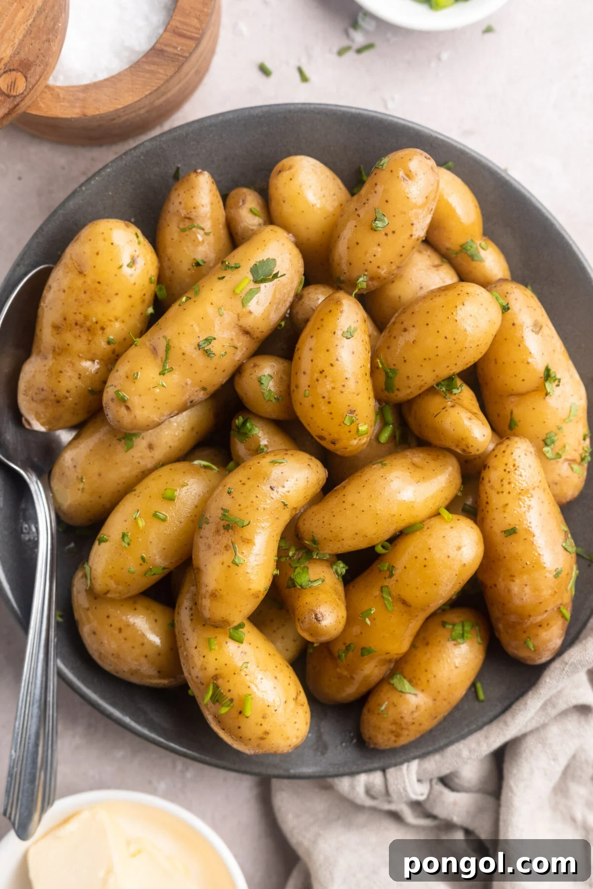 Overhead, top-down photo of sous vide fingerling potatoes in a shallow grey bowl. The brown potatoes are a little shiny and peppered with green herbs.