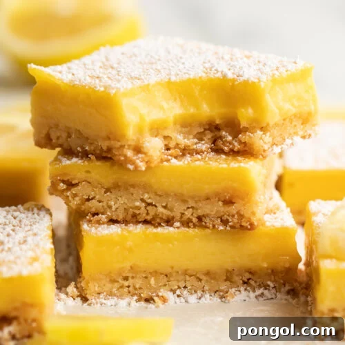 Three paleo lemon bars stacked on top of each other. A bite is missing from the corner of the lemon bar on top. Other lemon bars surround the stack, just out of focus.