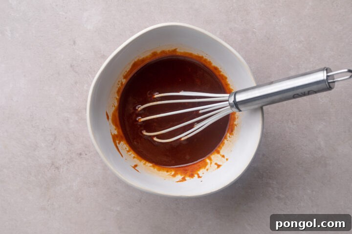 Sweet and Spicy Gochujang Sheet Pan Feast 7 Deep red gochujang sauce in a mixing bowl with a metal whisk, showing its smooth consistency.