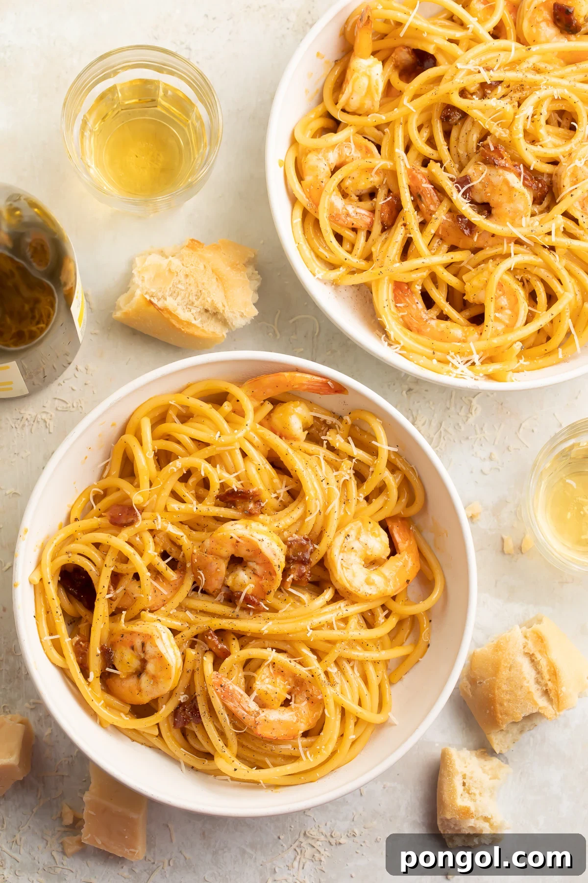 Top-down look at two bowls of shrimp carbonara, with linguini noodles swirled and piled to support tender shrimp.