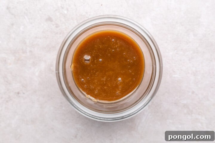 Keto caramel sauce in a glass jar on a neutral countertop.