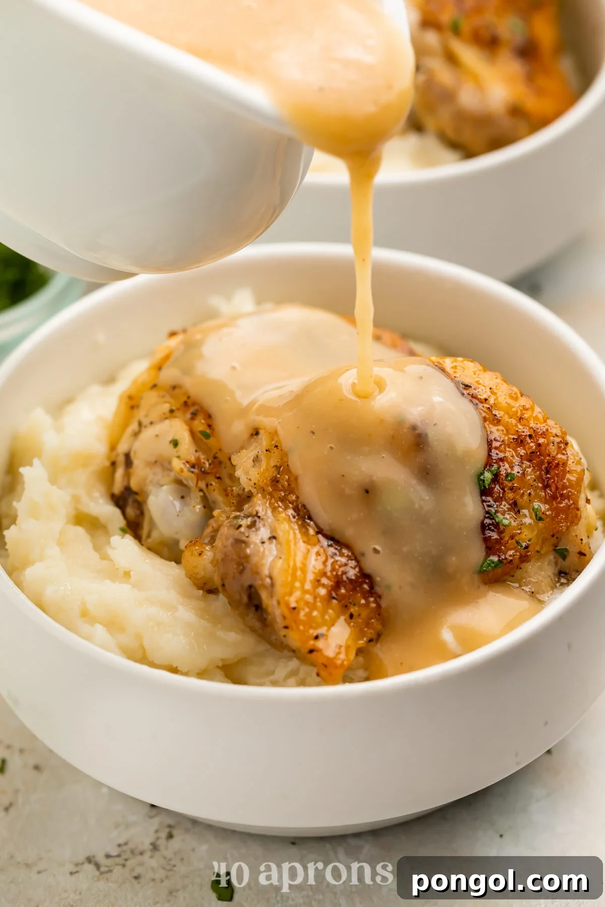 Gravy being poured over a perfectly cooked Instant Pot chicken thigh atop a bed of mashed potatoes in a bowl.
