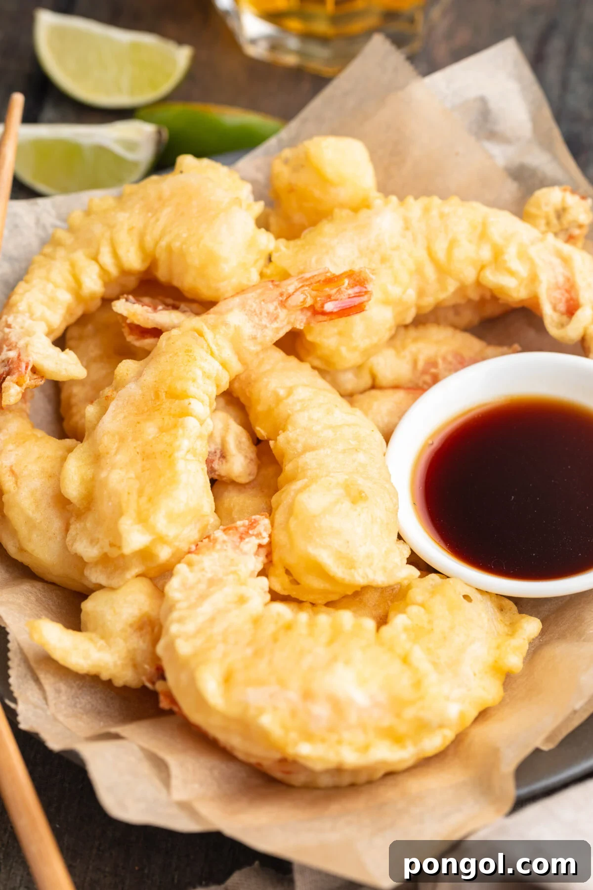 Golden Crispy Shrimp Tempura 2 A generous pile of freshly fried, light, and crispy shrimp tempura delicately placed on parchment paper, accompanied by a small bowl of traditional tempura dipping sauce, showcasing its golden perfection.