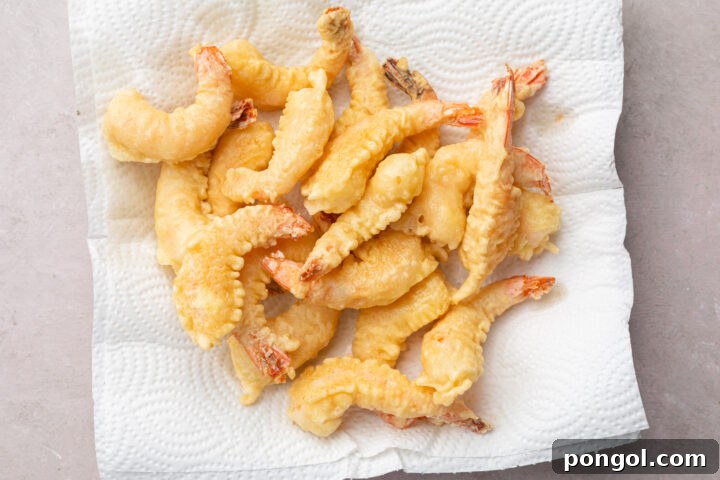 A fresh batch of golden-brown shrimp tempura resting on a wire cooling rack over paper towels, allowing excess oil to drain.