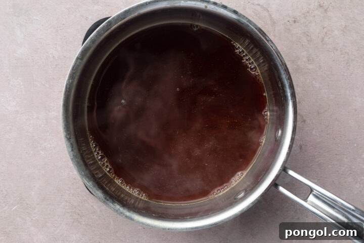 Tempura sauce simmering gently in a small silver saucepan, showing the added ingredients blending in.