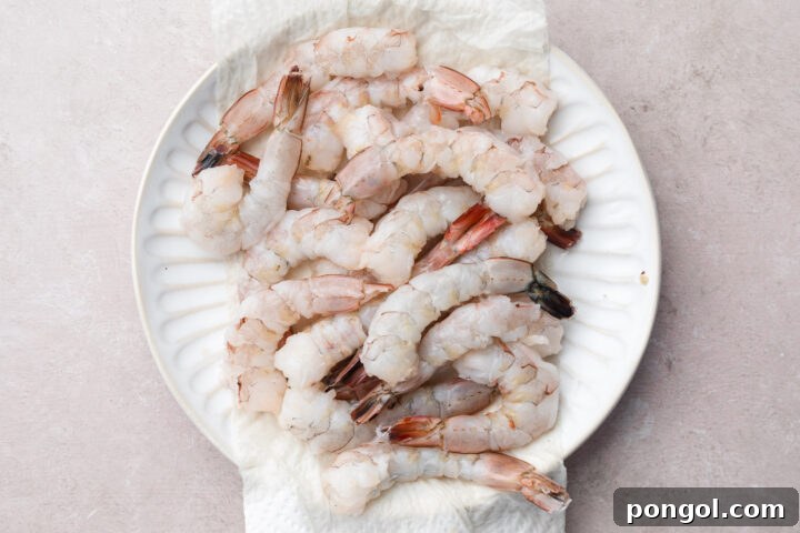 Large, peeled, and deveined shrimp, straightened with small slits on the underside, arranged neatly on a large plate.