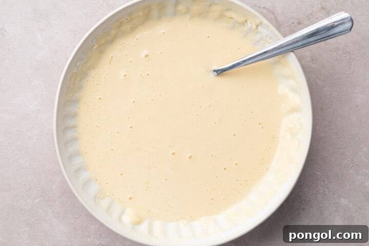 Prepared tempura batter, showing a slightly lumpy consistency in a shallow dish, ready for dipping shrimp.