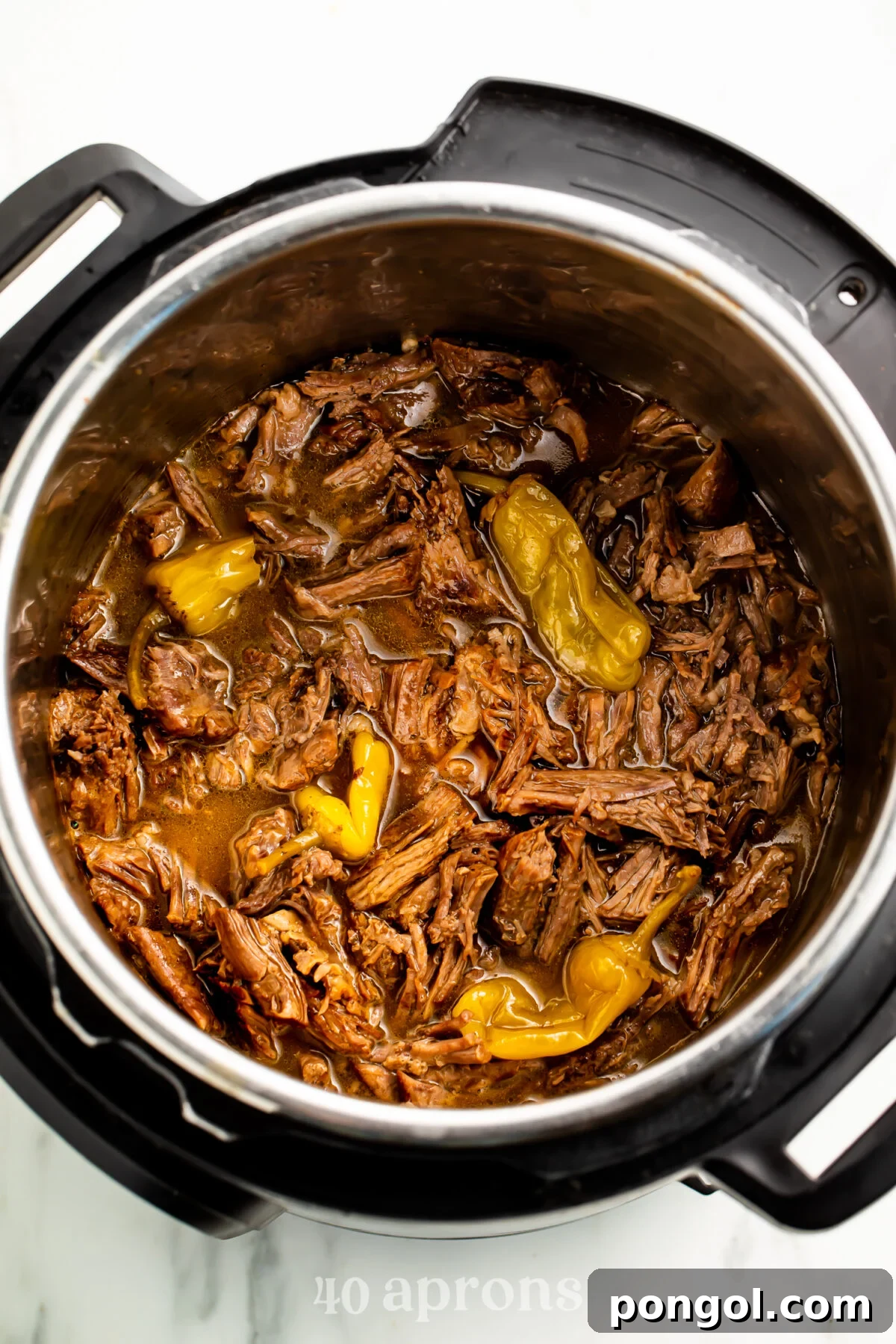 Overhead, top-down look at Instant Pot Mississippi pot roast in the Instant Pot. The rich, savory beef is nestled amongst pepperoncini peppers and swimming in a delectable gravy, showcasing its tender texture.