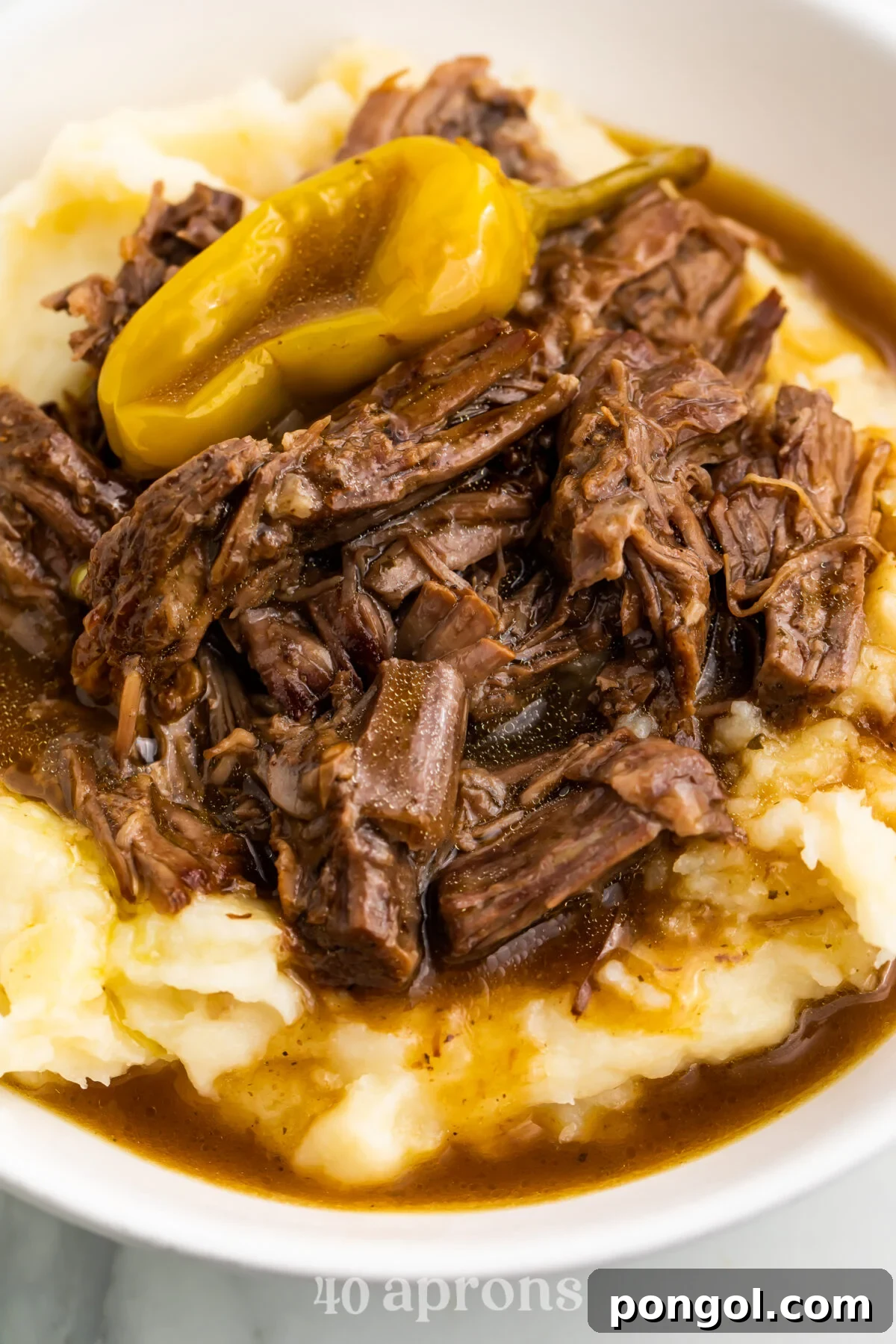 Instant Pot Mississippi pot roast served atop a creamy bed of mashed potatoes, generously drizzled with rich, savory pot roast gravy and garnished with vibrant pepperoncini.