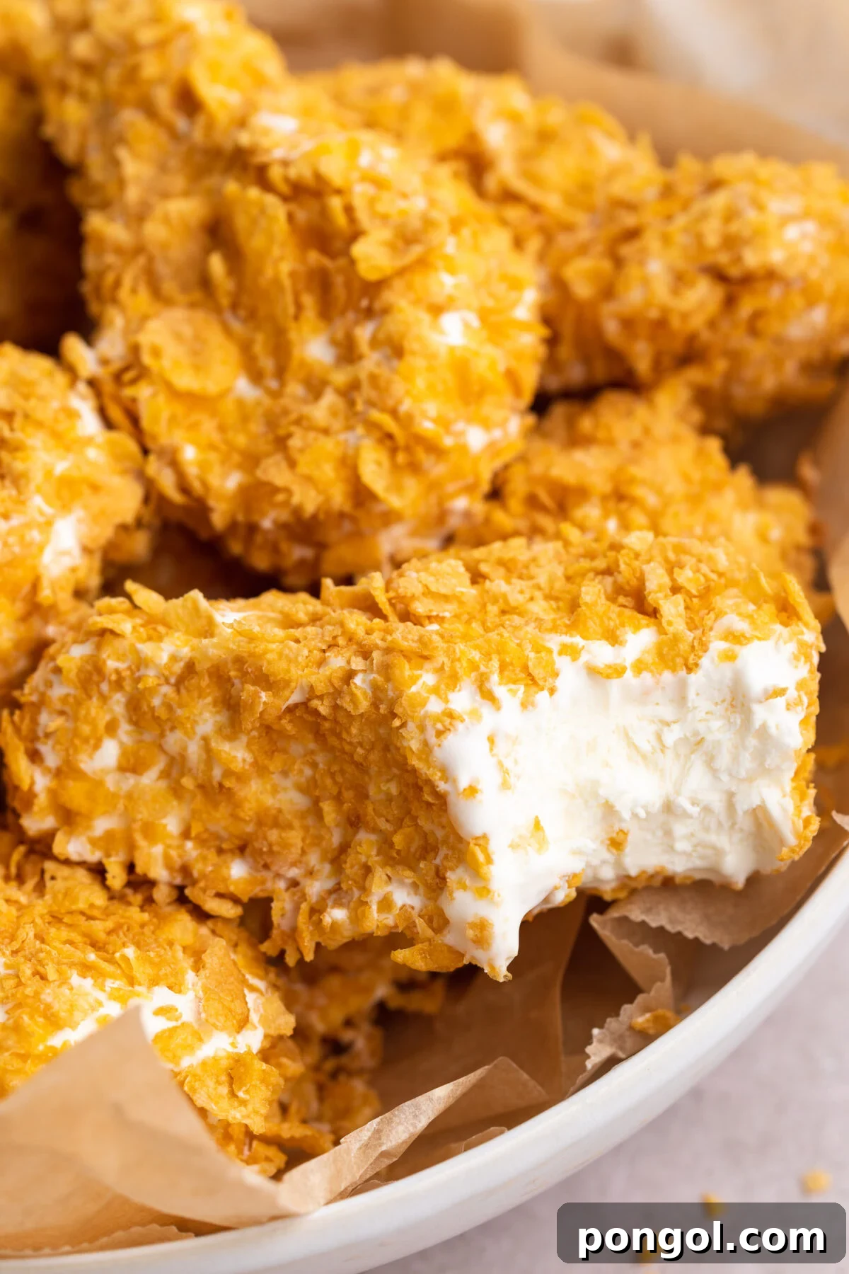 Fried chicken ice cream drumsticks coated in white chocolate and crushed cornflakes. A bite is missing from the forward-most drumstick, showing vanilla ice cream inside.