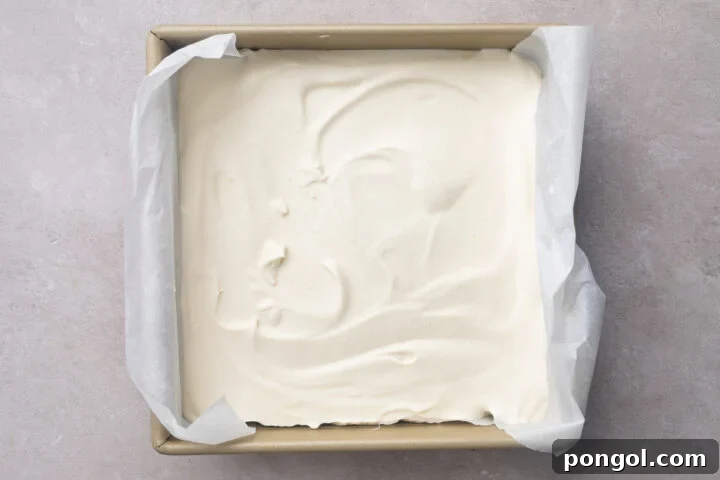 Top-down look at homemade vanilla ice cream in an 8x8 square baking pan lined with parchment paper.