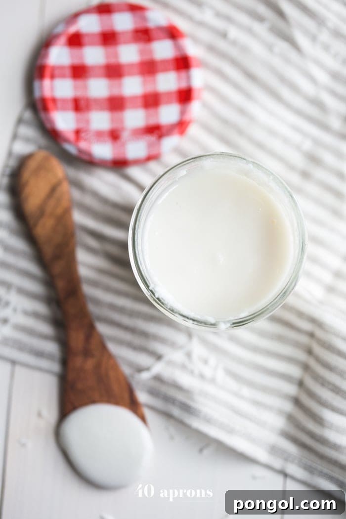 A jar of freshly made, silky coconut butter sits beside a blender, with a spoon dipped in, showing its smooth, spreadable consistency.