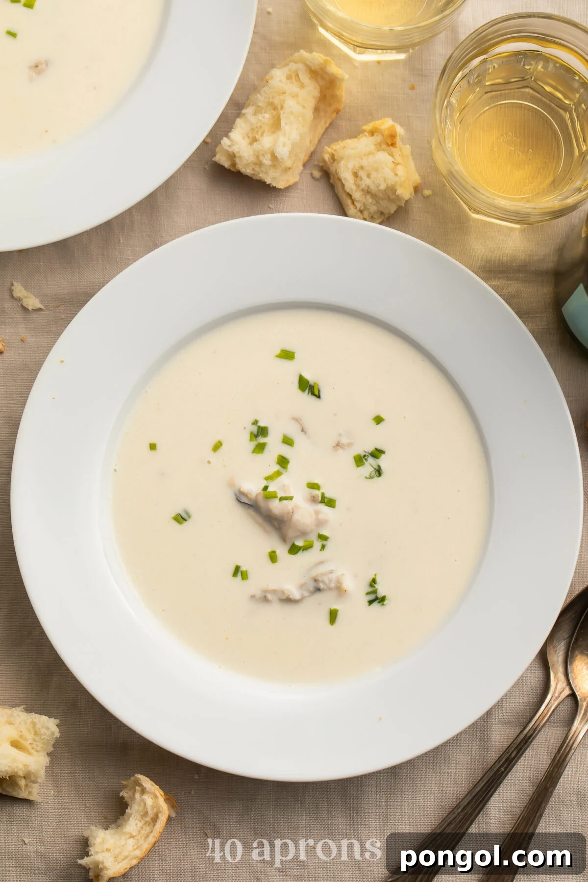A pristine white, restaurant-style bone soup bowl holds a creamy, pale oyster brie soup, elegantly dotted with vibrant green chives for garnish.