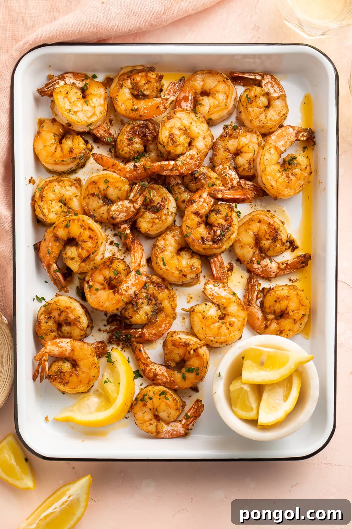 Garlicky, buttery broiled shrimp in a roasting pan on a pink tablecloth.