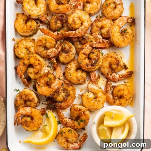 Garlicky, buttery broiled shrimp in a roasting pan on a pink tablecloth.