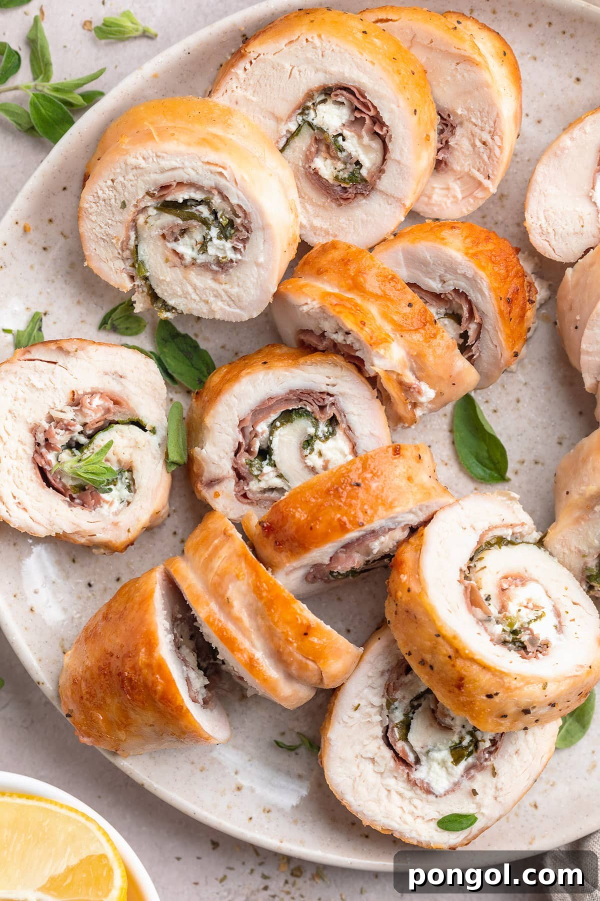 Several slices of chicken roulade, stuffed with prosciutto, spinach, and goat cheese, on a neutral plate.