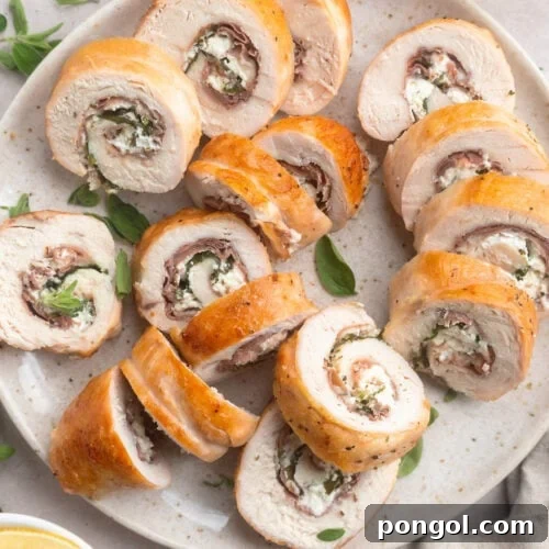 Several slices of chicken roulade, stuffed with prosciutto, spinach, and goat cheese, on a neutral plate.