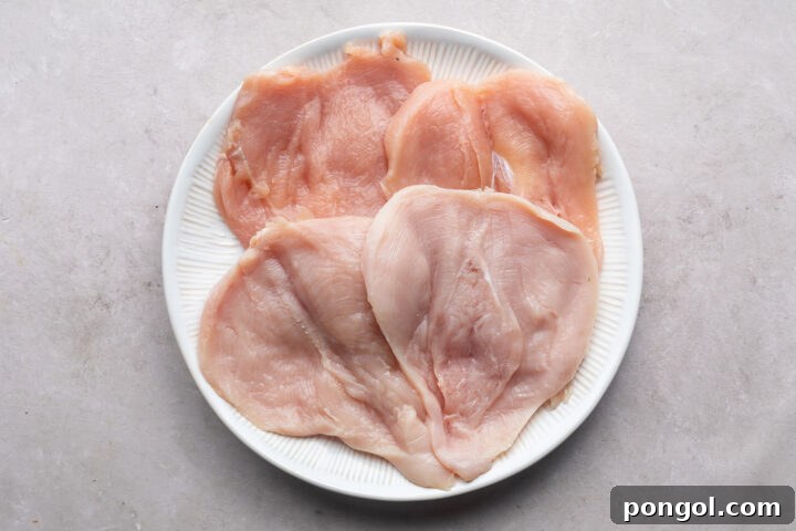 Butterflied chicken breasts on a round white plate.