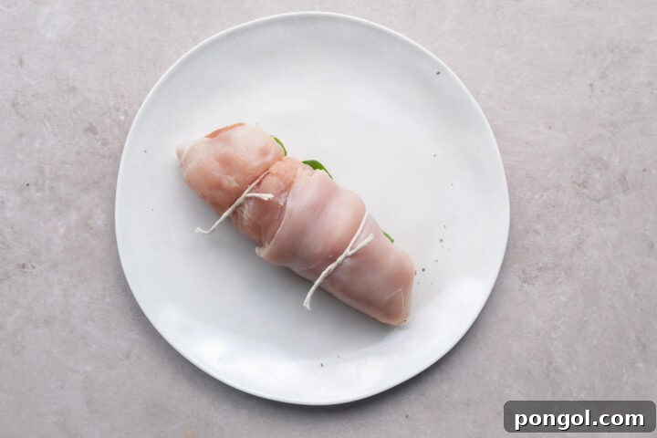 Chicken roulade tied with butcher's twine and resting on a white plate.