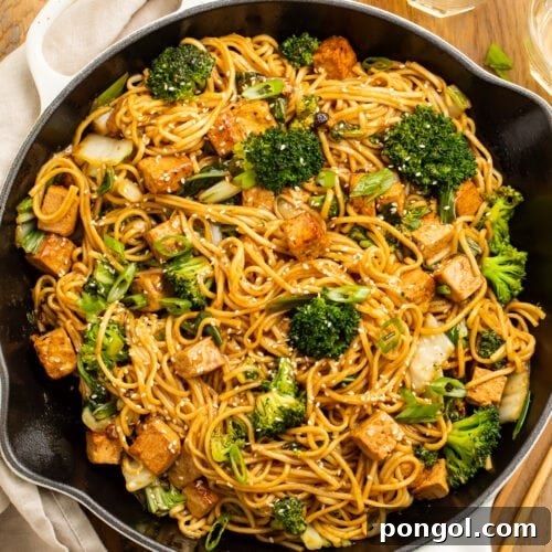 Zoomed out over head view of stir fry noodles with tofu and veggies in a large skillet.